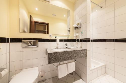 a bathroom with a sink and a toilet and a mirror at Garner Hotel Cologne Porz - Airport by IHG in Cologne
