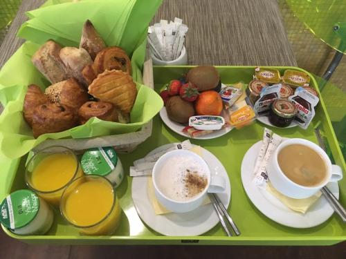 a green tray of food with cups of coffee and pastries at Hôtel Le Fabe in Paris