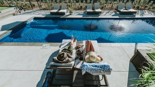 two people laying on lawn chairs near a swimming pool at Villas Waiheke in Onetangi