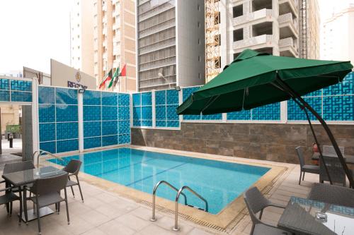 a swimming pool with tables and chairs and a green umbrella at Regent Hotel Apartments in Kuwait