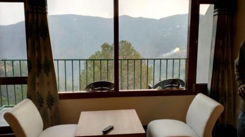 a room with a table and chairs and a large window at Hotel Emerald Valley in Chail