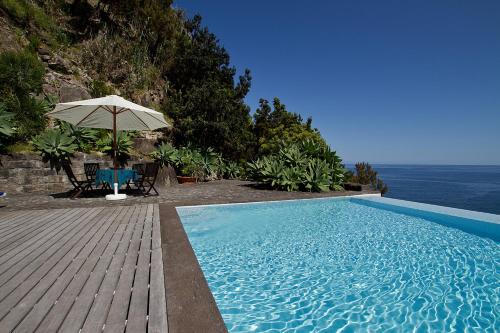 a swimming pool with an umbrella and a table and chairs at Casa de Pedra in Ribeira Quente