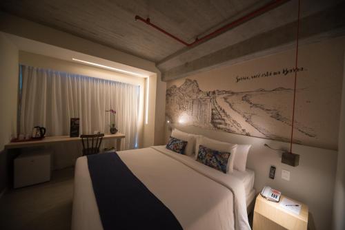 a hotel room with a bed, desk and a painting on the wall at Ramada Encore by Wyndham Rio de Janeiro Ribalta in Rio de Janeiro