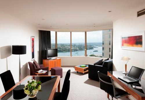 a living room with a desk and a living room with a view at The Sebel Quay West Suites Sydney in Sydney