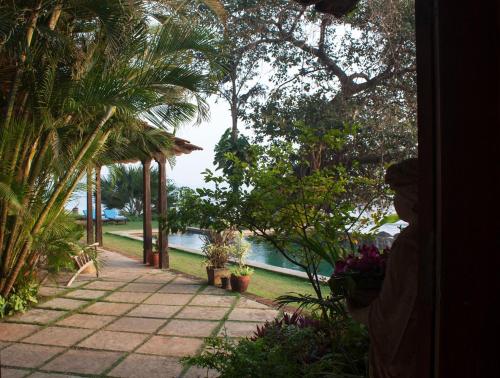 a garden with palm trees and a walkway next to the water at Ahilya By The Sea in Nerul