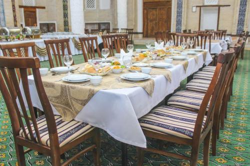 a long table with chairs and plates of food on it at Orient Star Khiva Hotel- Madrasah Muhammad Aminkhan 1855 in Khiva