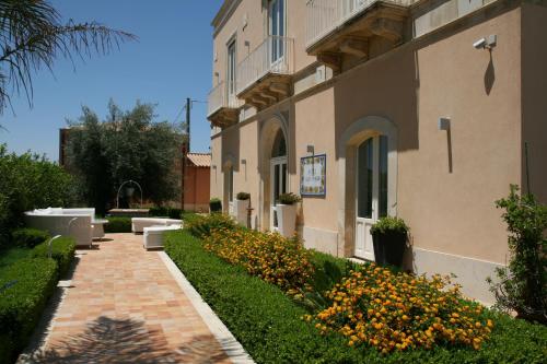 a building with a walkway and flowers in front of it at Hotel Villa Fanusa in Siracusa