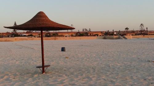 a straw umbrella in the sand on a beach at El Zohour Chalet North Coast in El Alamein