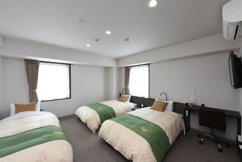 a room with three beds and a desk and windows at Hotel Showmeikan in Mishima