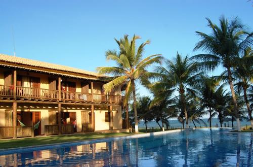 a resort with a swimming pool and palm trees at Pousada Praia das Ondas - Pé na areia in Itacimirim