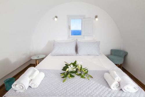 Una cama blanca con toallas y una planta. en Evilio Houses, en Oia