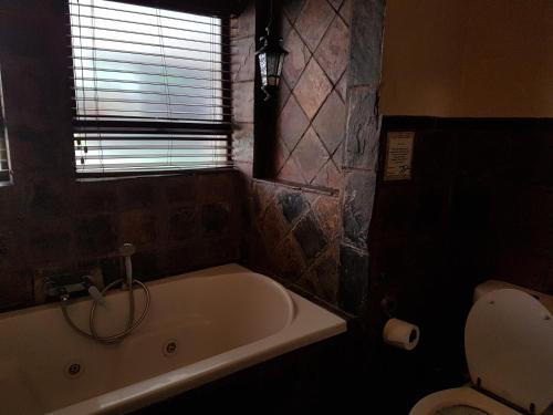 a bathroom with a tub and a toilet and a window at Santai guesthouse in Brits