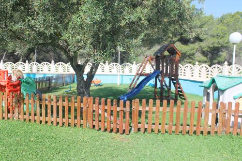 a wooden fence with a playground in front of a pool at Aparthotel Bahia Pinosol in Jávea