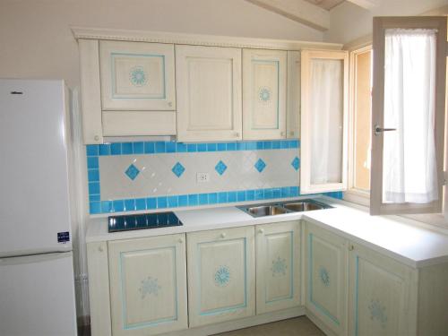 カステルサルドにあるAttico Romaの白いキャビネットと青いタイルの壁が備わるキッチン