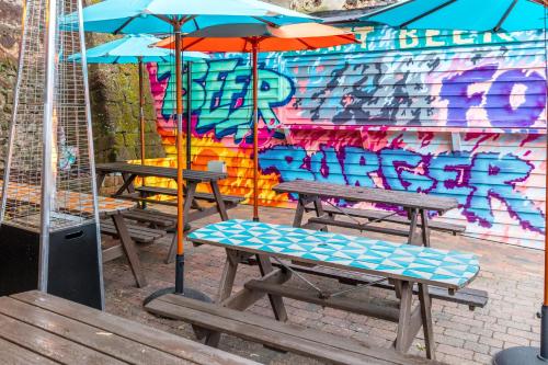 two picnic tables with umbrellas in front of a wall with graffiti at City Gate in Exeter