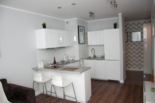 Biała kuchnia z białymi szafkami i stołkami barowymi w obiekcie Apartament Garazowa 5 w Warszawie