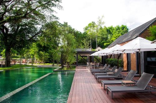 a swimming pool with lounge chairs and umbrellas at Flora Creek Chiang Mai in Hang Dong