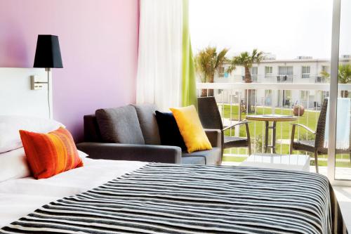 a hotel room with a bed and chairs and a balcony at Sunprime Ayia Napa Suites - Adults Only in Ayia Napa