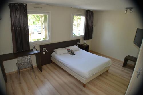 a bedroom with a bed and a desk and two windows at Hotel Primo Colmar Centre in Colmar