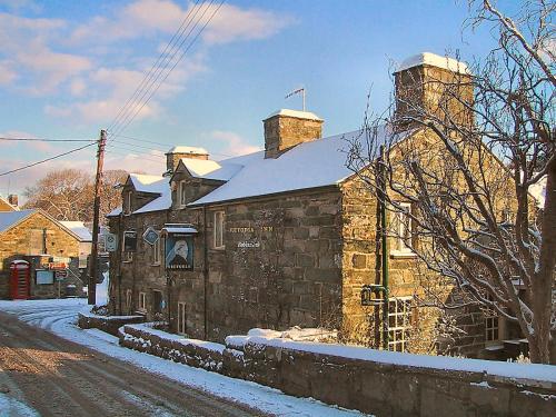 a stone building with two chimneys on a snowy street at Victoria Inn in Llanbedr
