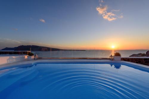 a large swimming pool with the sunset in the background at Ode Villa in Oia