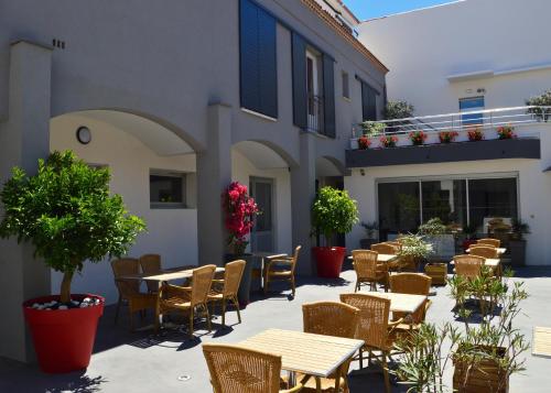 an outdoor patio with tables and chairs and plants at Hotel Les Acacias in Le Grau-du-Roi