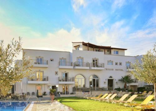 a large white building with chairs in front of a pool at Frixos Hotel in Malia
