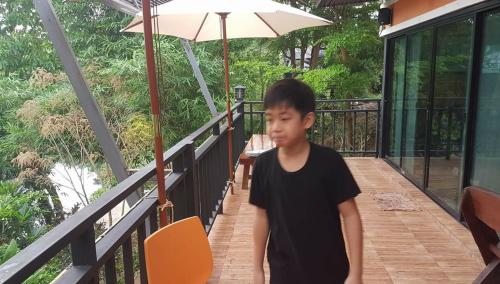 a young boy standing on a balcony with an umbrella at Kaengkrachan River Hut in Kaeng Krachan