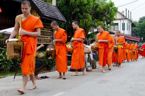 een groep monniken in oranje gewaden die door een straat lopen bij Villa Chitdara in Luang Prabang