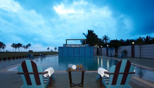 twee stoelen en een tafel naast een zwembad bij RNS Golf Resort & Nature Cure Centre in Māvalli