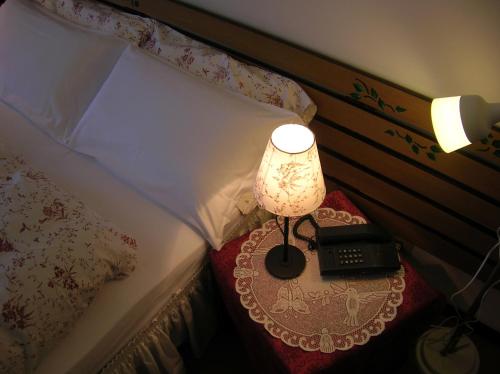a bed with a table with a lamp and a telephone at HG Hotel La Caminatha in Val di Zoldo