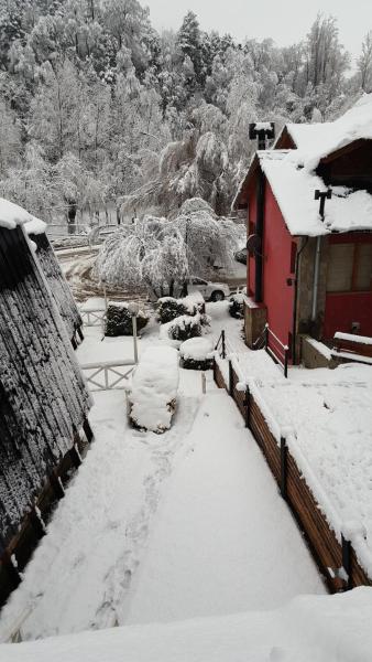 un patio cubierto de nieve con un edificio rojo y una casa en Villa El Radal en San Martín de los Andes