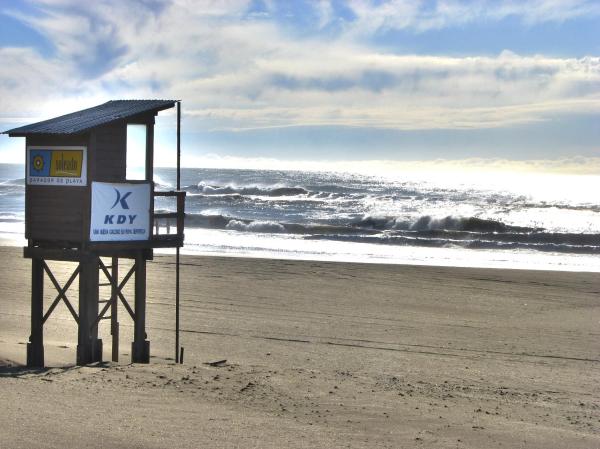 un cartel en una playa con el océano al fondo en Del Lucero en Mar de las Pampas