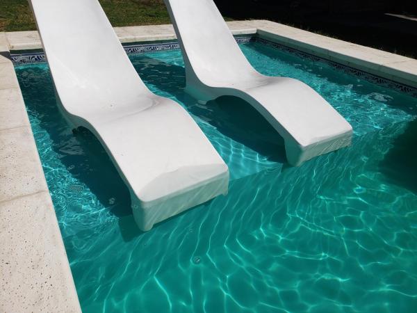 una piscina con 2 sillas blancas en el agua en Comoda casa en el centro de Villa Carlos Paz, pileta privada, cinco minutos a pie de la peatonal, aire, porton electrico, en Villa Carlos Paz