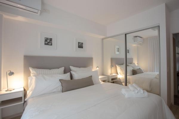 1 dormitorio blanco con 1 cama blanca grande y espejo en BAIRES HOMES PALERMO III en Buenos Aires