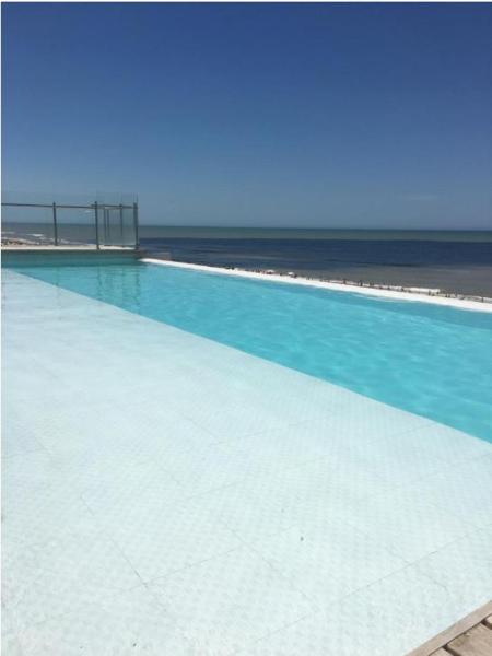 una gran piscina de agua azul y la playa en Los Pinos Pinamar en Pinamar