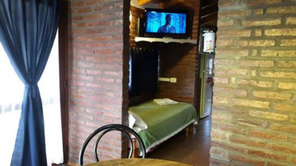 Habitación con cama y TV en una pared de ladrillo. en Cabañas de las Mellizas, en Villa Carlos Paz