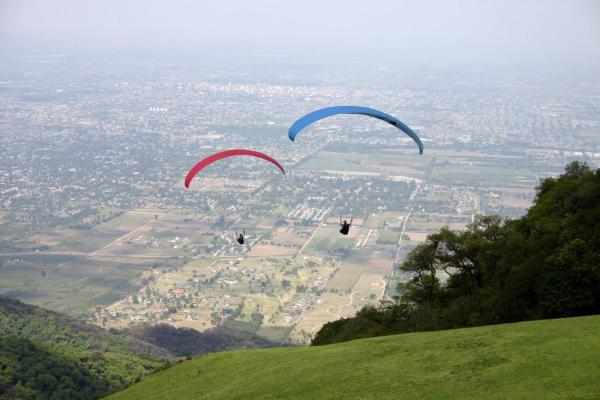 dos parapentes están volando sobre una colina verde en B and B Marcos Paz Apartment en San Miguel de Tucumán