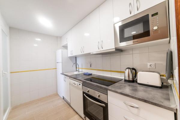 una pequeña cocina con armarios blancos y microondas en Moonkey - Apartamento Las Mandarines, en Benidorm