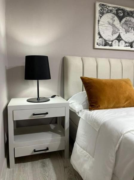 Una cama con mesita de noche con una lámpara. en Altos de Pinamar en Ostende