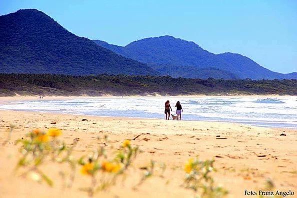 two people walking on a beach near the ocean at Olhar da Barra Hospedagem - Refugio Urbano I in Florianópolis