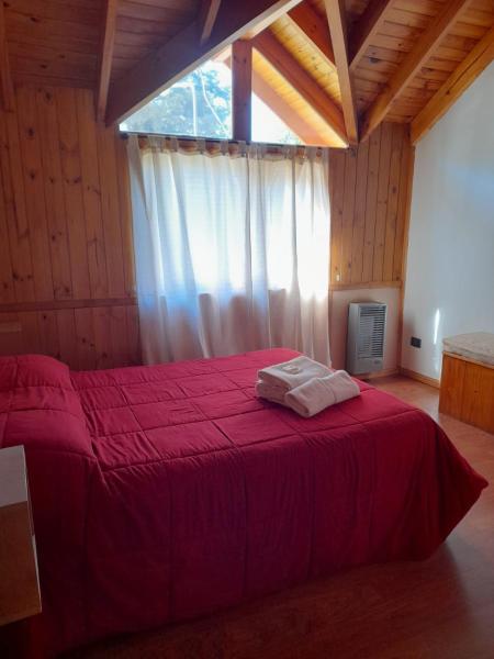 1 dormitorio con cama roja y ventana grande en Departamentos Sonne Depto Planta Alta en San Martín de los Andes