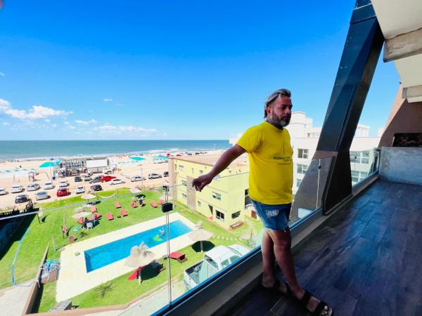 un hombre parado en un balcón con vistas a la playa en Departamentos Sobre el Mar en Villa Gesell