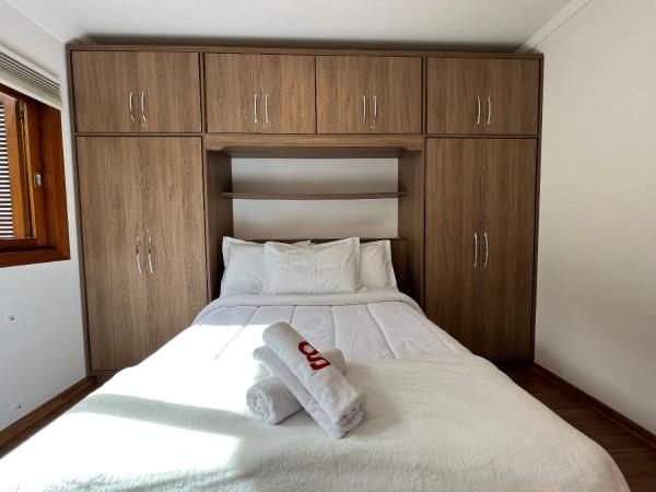 1 dormitorio con 1 cama blanca grande y armarios de madera en Vista do Quilombo 204B - Apartamento no Centro de Gramado, en Gramado