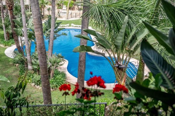 una piscina en un complejo con palmeras y flores rojas en FA- Luxury 2 bedroom apt Fuente Aloha, en Marbella