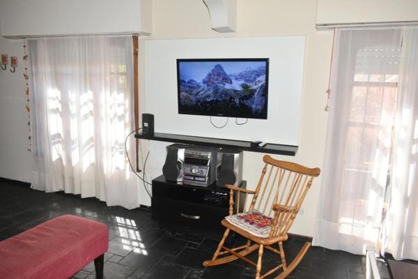 Sala de estar con silla y TV en la pared en Villa Hilda - Casa con Pileta en Tandil