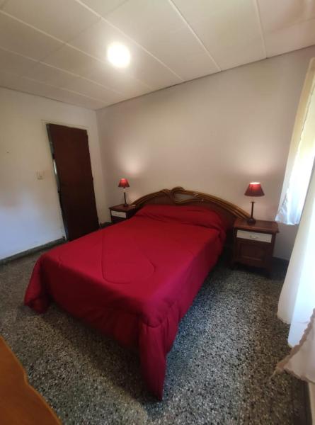 1 dormitorio con 1 cama grande de color rojo y 2 mesas en Departamentos Pablos A Villa Gesell en Villa Gesell