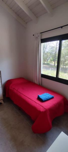 Cama roja en habitación con ventana en Villa General Belgrano Inbalo 01 en Villa General Belgrano