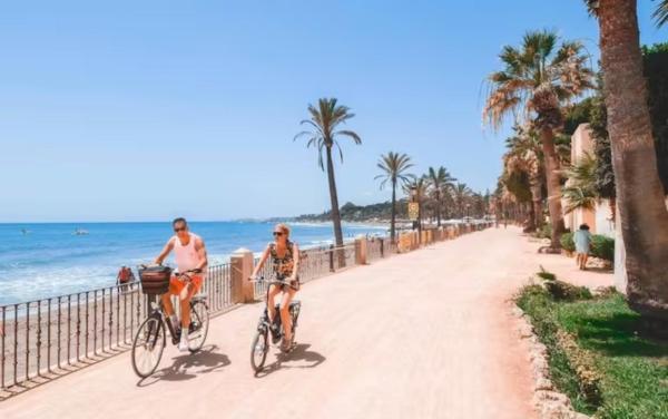 dos personas montando en bicicleta por una acera cerca de la playa en Duplex con encanto bahía, en Marbella