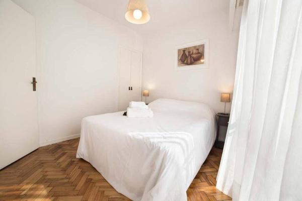 Cama blanca en una habitación con paredes blancas y suelo de madera. en Cozy apartment great location en Buenos Aires